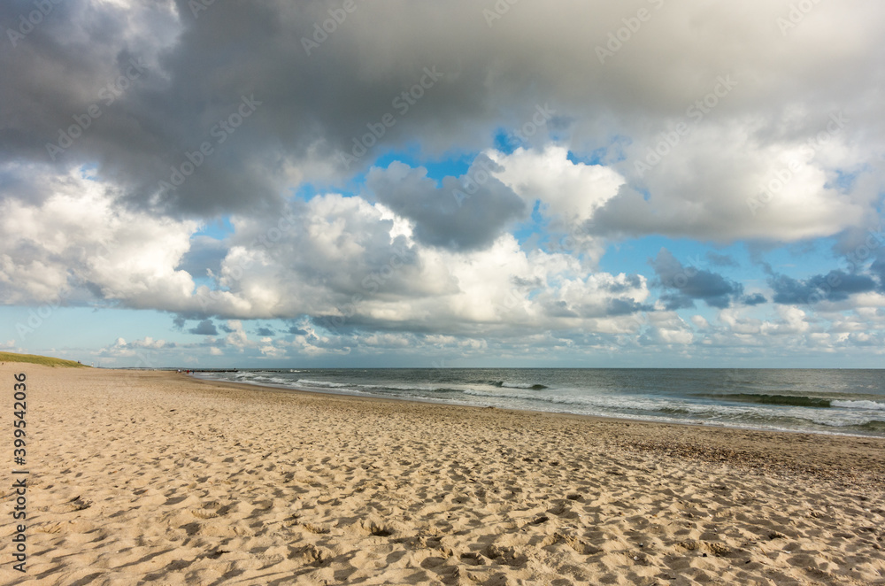 Beach sand with blue sky and dramatic clouds at coastline waterfront in soft evening sunset light. Hvidbjerg Strand, Blavand, North Sea, Denmark.