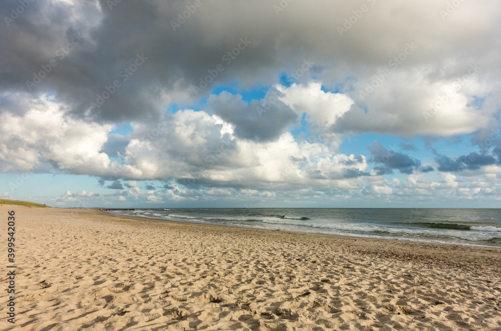 Beach sand with blue sky and dramatic clouds at coastline waterfront in soft evening sunset light. Hvidbjerg Strand, Blavand, North Sea, Denmark. Beach sand with blue sky and dramatic clouds at coastline waterfront in soft evening sunset light. Hvidbjerg Strand, Blavand, North Sea, Denmark.