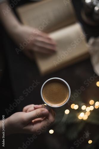 Cup of espresso in the girl's hand and a book, dark photo, selective focus, cozy evening photo, top view