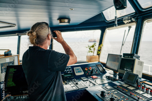 Captain deck Officer on bridge of vessel or ship. He is looking through binoculars. COLREG navigaton watch at sea