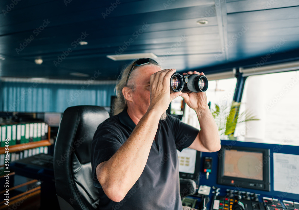 Captain deck Officer on bridge of vessel or ship. He is looking through binoculars. COLREG navigaton watch at sea