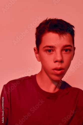 Close up portrait of teenaged disabled boy with cerebral palsy looking away, posing isolated over red light background