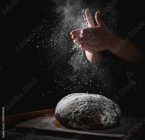 woman chef hand clap with splash of white flour and black background with copy space. woman s hands Making bread