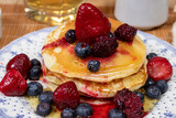 Stack of homemade pancakes prepared with blueberries, strawberries and maple syrup or honey dripping pancakes on an old plate on a wooden table. Concept healthy food at breakfast.