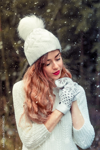 A girl in a white hat and warblers is warming up, it is snowing. winter.