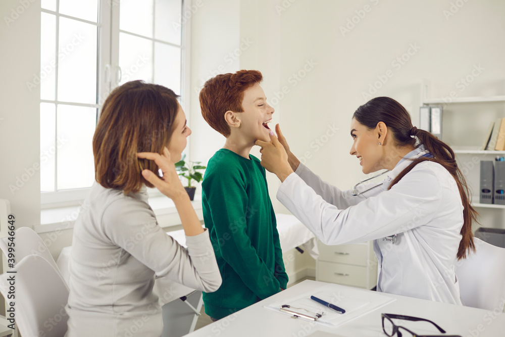 Pediatrician woman checks for sore throat of a boy who came for an examination with his mother.