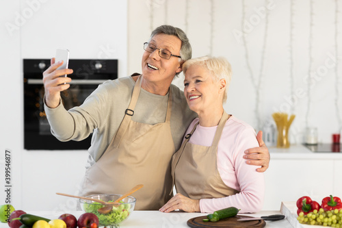 Cheerful Senior Couple Making Selfie On Cellphone Cooking In Kitchen