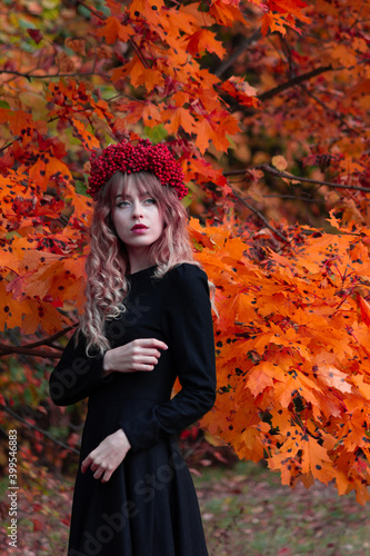 Beautiful girl in a black dress in a wreath of mountain ash in the autumn forest.
