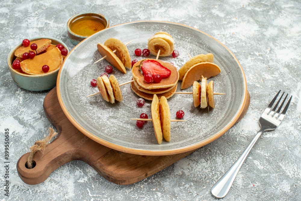 Side view of delicious pancakes with fruits on wooden cutting board and honey on blue background