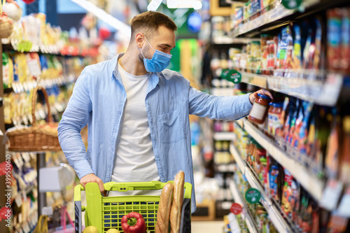 Young man in face mask with cart shopping in hypermarket