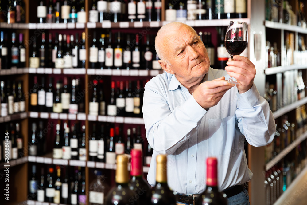 Older man inspecting quality of red wine in wine store in search of perfect wine for solemn occasion. High quality photo