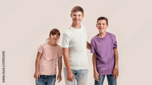 Three teenaged disabled children with Down syndrome and cerebral palsy smiling at camera while posing together isolated over white background