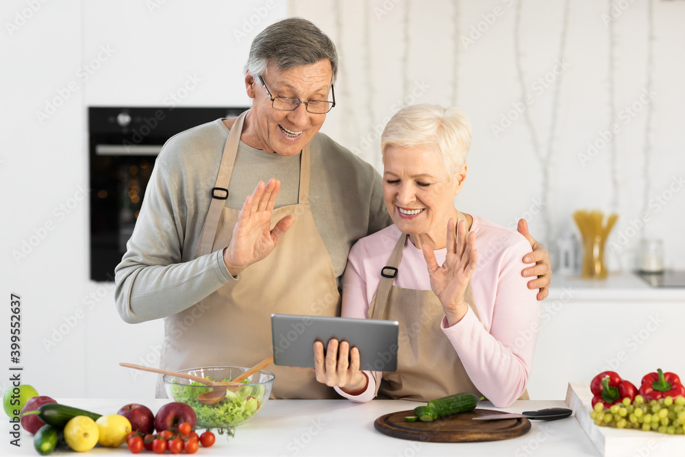 Senior Couple Video Calling Using Digital Tablet Standing In Kitchen