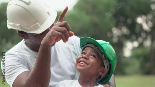 Cheerful african american father and son in hard hat playing in park, Happiness family concepts, parent and child play in park