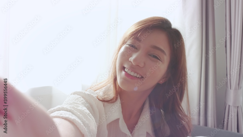 Lovely Asian girl smiling and show her hand in a white shirt takes a video selfie call with a friend in the sunlight color soft stay Lovely Asian girl smiling and show her hand in a white shirt takes a video selfie call with a friend in the sunlight color soft stay