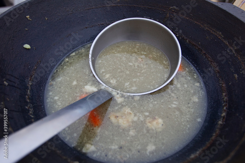 Large scoop in a vat or pot of soup. Street food.