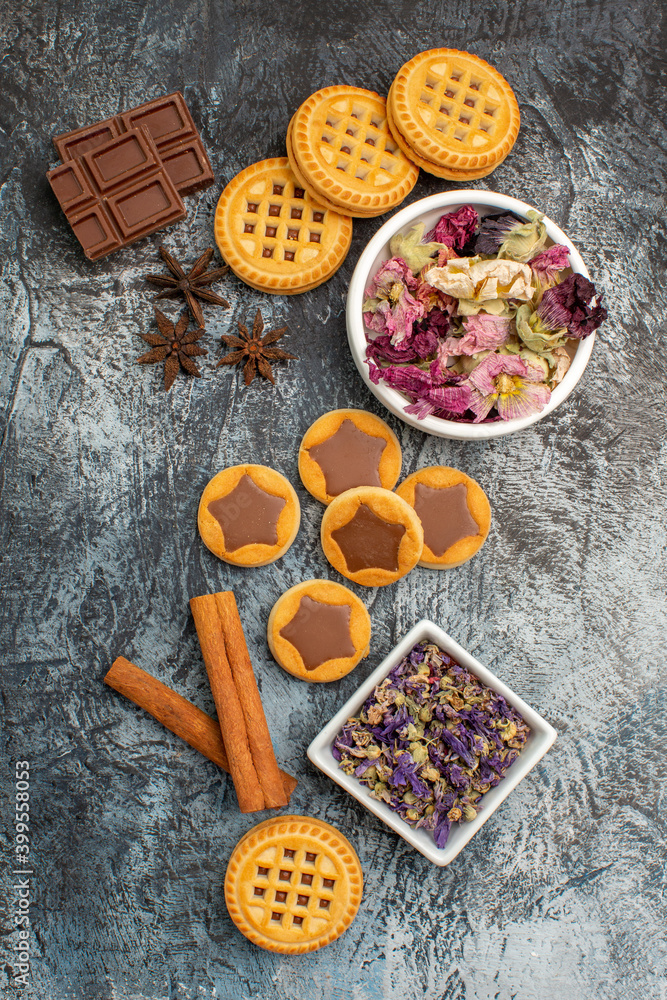 top view of bowls of dry flowers with cookies and cinnamons on the right side of grey ground top view of bowls of dry flowers with cookies and cinnamons on the right side of grey ground