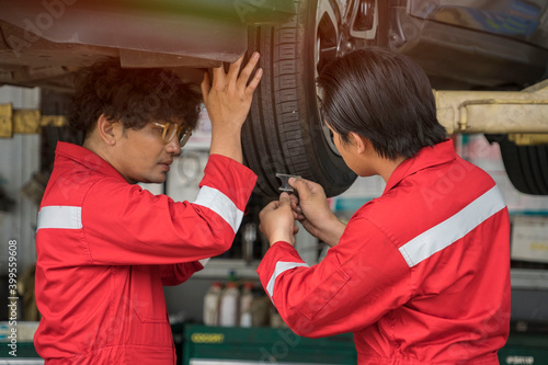 Technicians team to fix cars, wear red uniforms, use tools to measure tires in the garage. 