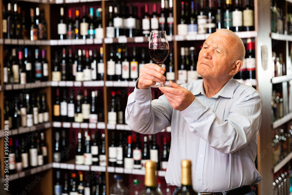 Older man inspecting quality of red wine in wine store in search of perfect wine for solemn occasion. High quality photo