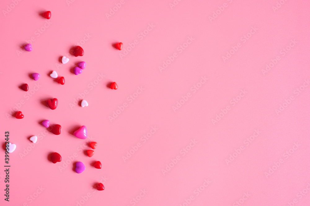 a heap of heart shaped glossy beads in different pink shades on a pink background. space for text