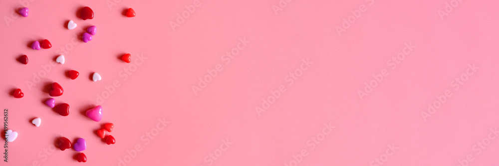 a heap of heart shaped glossy beads in different pink shades on a pink background. banner. space for text