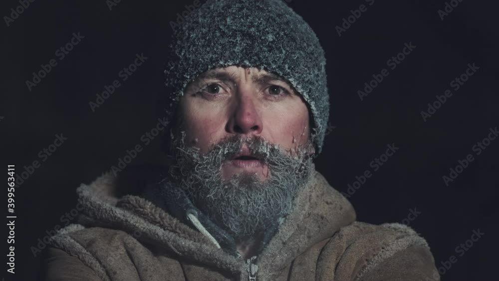Man with frozen face. Young adult man with icy beard and hat breathes outdoor at subzero temperatures environment Man with frozen face. Young adult man with icy beard and hat breathes outdoor at subzero temperatures environment