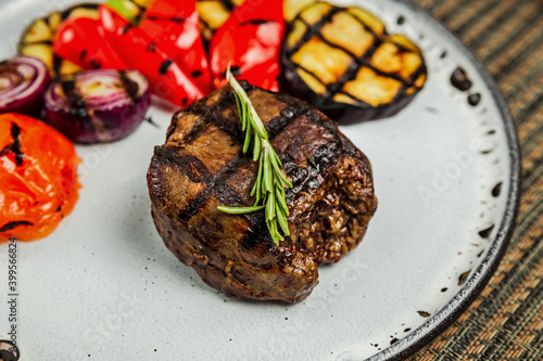 Filet mignon with grilled vegetables and rosemary garnish on a white plate, close-up © jamurka