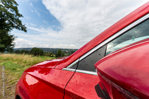 Side view of a red car with the left-hand side mirror in focus. Rain drops are visible too