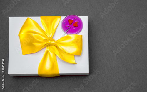 White gift box with bow and lollipop on gray background. Copy space
