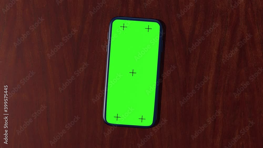 Black smartphone with green screen slides on a brown wooden table. Motion cell (mobile) phone on wood background. Close up 3d animation of telephone on desktop with chroma key. Top view. 4k. Black smartphone with green screen slides on a brown wooden table. Motion cell (mobile) phone on wood background. Close up 3d animation of telephone on desktop with chroma key. Top view. 4k.
