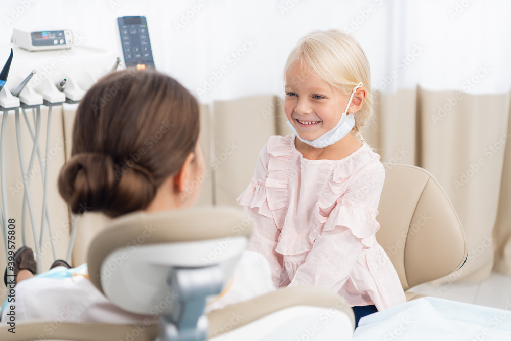 Obraz premium Adorable little girl sitting and making an examination of a female doctor, the doctor is sitting in a dentist chair. Dentist and child in a dentist office. Little girl in the dentists office.