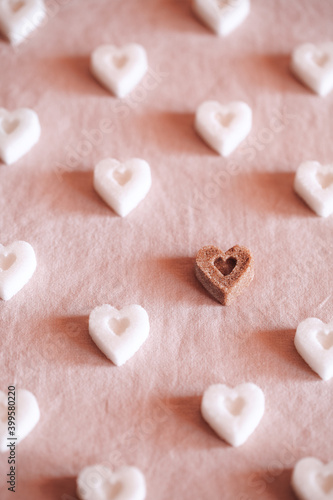 White heart shaped sugar and one brown on pink textile background. Valentines Day concept