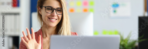 Portrait of smiling lovely lady waving hello talking on video call. Successful young woman sitting in pink jacket. Blonde happy worker. Business conference via laptop. Job concept