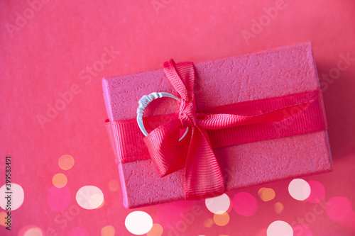 A ring made of precious metal and stone lies on a gift box. Defocused light.