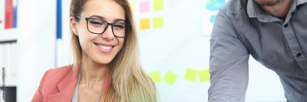 Portrait of smiling beautiful young woman wearing stylish pink jacket on working place. Female talking to male employee. Creative job and business agency concept Portrait of smiling beautiful young woman wearing stylish pink jacket on working place. Female talking to male employee. Creative job and business agency concept
