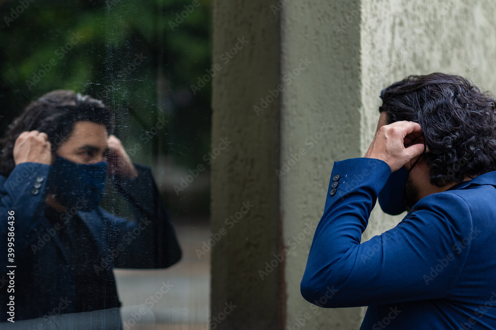Homem elegante, colocando máscara e olhando seu próprio reflexo no vidro de prédio.