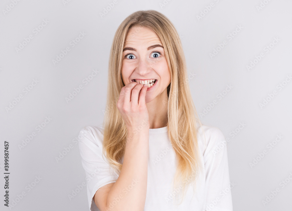 Close up portrait of a worried blonde girl in white t-shirt biting her nails isolated over white background Close up portrait of a worried blonde girl in white t-shirt biting her nails isolated over white background