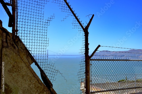 View from Alcatraz Island in San Francisco Bay towards Golden Gate Bridge, torn fence, blue sky background