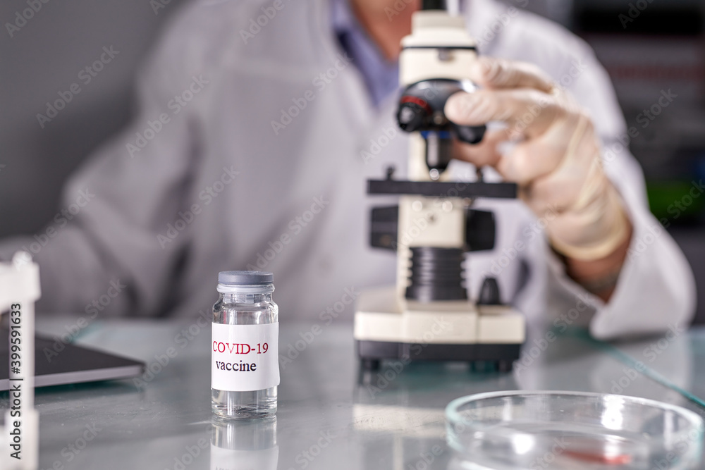 close-up photo of vaccine in bottle and microscope in lab, focus on vaccine bottle. covid-19, flu concept close-up photo of vaccine in bottle and microscope in lab, focus on vaccine bottle. covid-19, flu concept