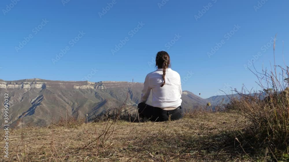 brunette woman in a white shirt sits on the ground under a clear sky in the mountains. brunette woman in a white shirt sits on the ground under a clear sky in the mountains.