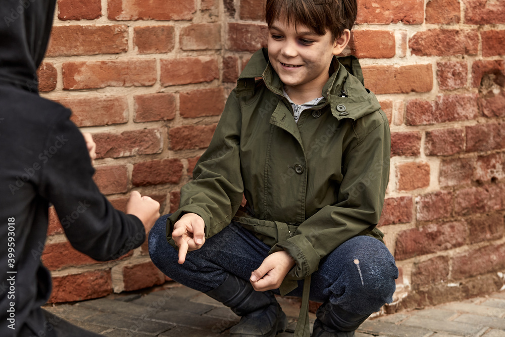 two friendly street boys playing games on street, caucasian children in dirty clothes have fun despite poverty