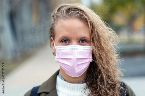 Beautiful young woman in pink face mask standing in the street looking at camera.