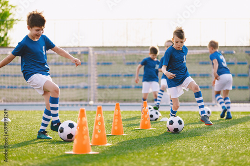 Young footballer improving dribbling skills on turf football training pitch. Kids in sportswear play ball sports