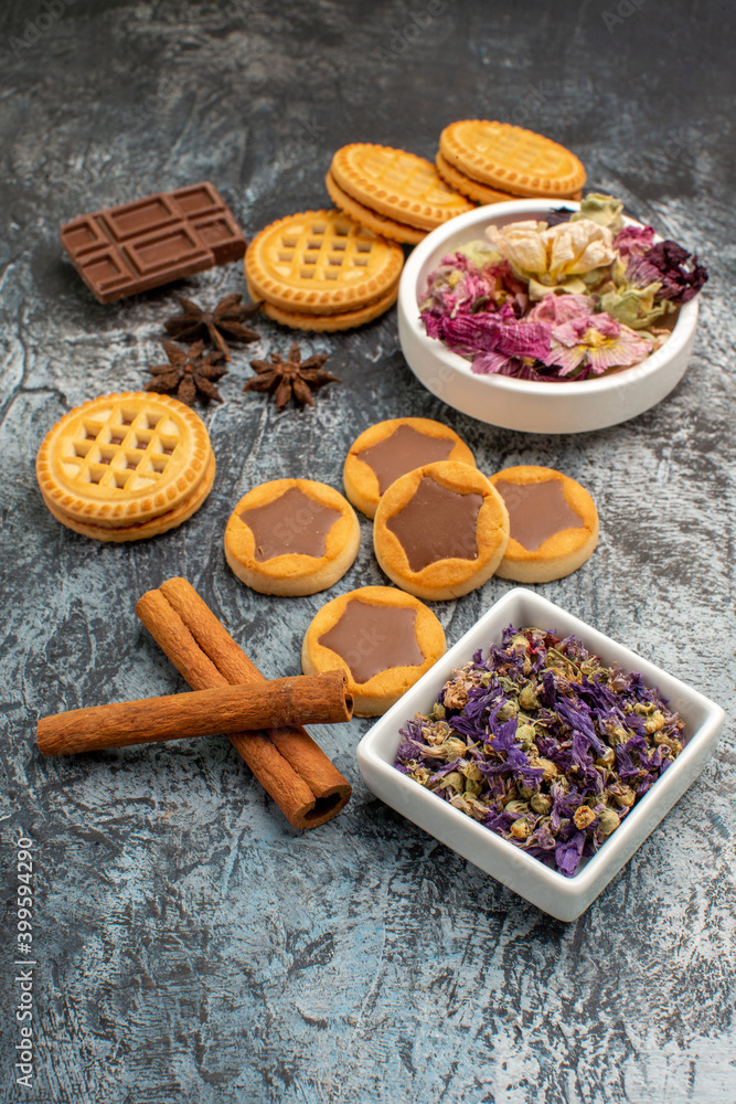sidewise view of cookies on wooden platter and chocolates and bowls of dry flowers on grey ground sidewise view of cookies on wooden platter and chocolates and bowls of dry flowers on grey ground