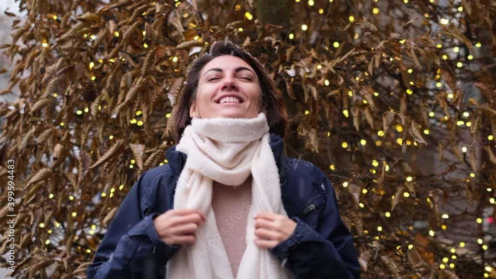 Happy woman wearing scarf outside enjoying first snow, stands by christmas tree Happy woman wearing scarf outside enjoying first snow, stands by christmas tree