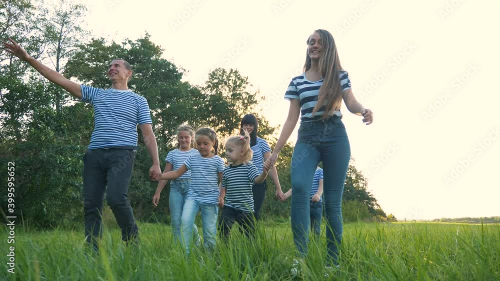Happy cute family is walking in a green park. A friendly family with children walks in the fresh air. Cute kids, mom and dad are having fun together in the park. Father of many children Happy cute family is walking in a green park. A friendly family with children walks in the fresh air. Cute kids, mom and dad are having fun together in the park. Father of many children