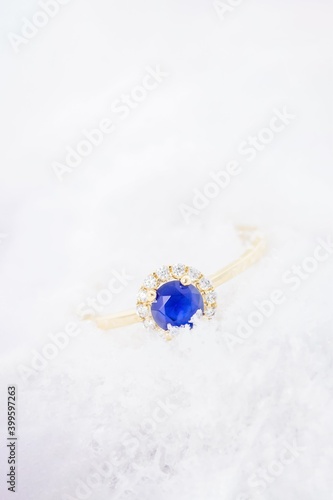 Gold ring with blue sapphir on white snow background photo