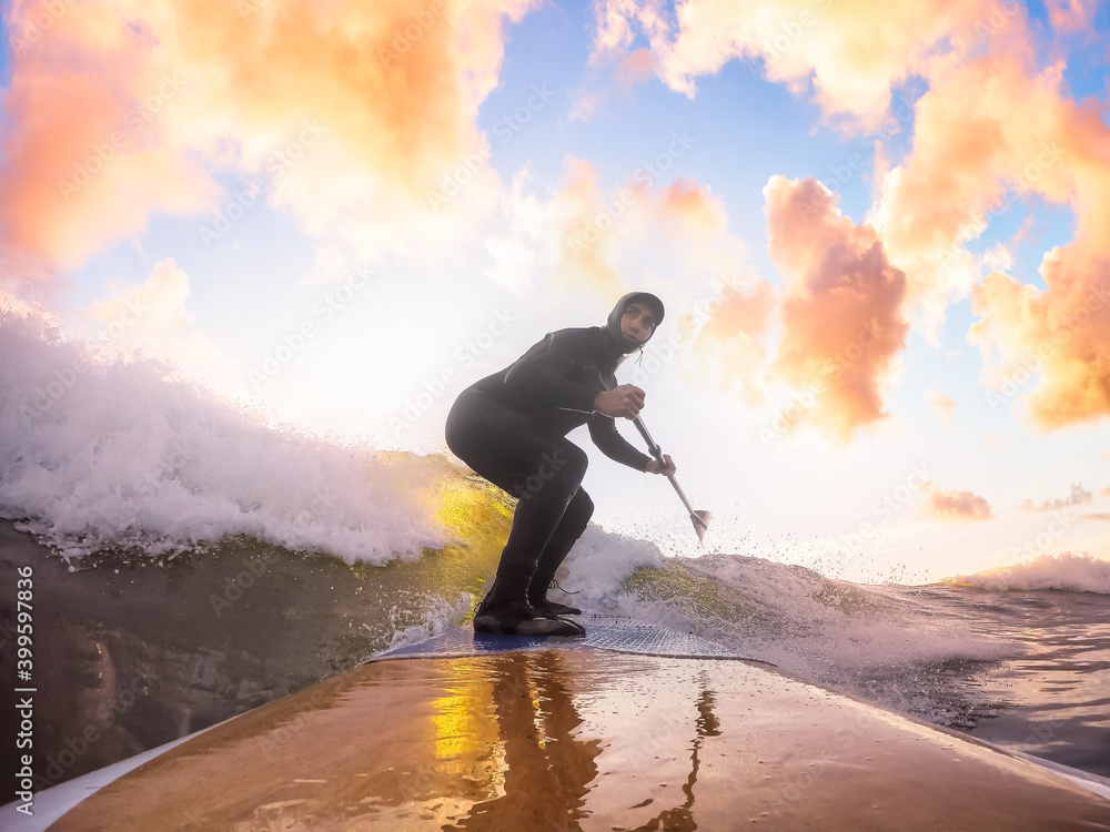 Obraz premium Adventurous Man Surfing the waves at the Pacific Ocean in Tofino, Vancouver Island, British Columbia, Canada. Dramatic Colorful Sunset Sky. Extreme sport