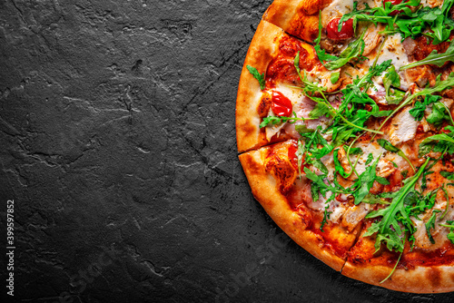 Pizza with chicken, bacon, cheese, tomato and arugula. Italian pizza on Dark grey black slate background