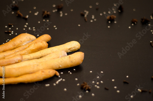 Ruddy grissini, dry long bread with sesame seeds, on a black background with spices, star anise and cloves, with copyspace